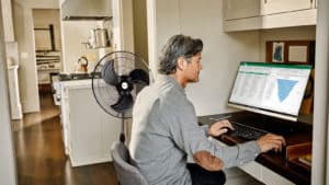 Señor trabajando en su computadora resfrescándose con un ventilador airon